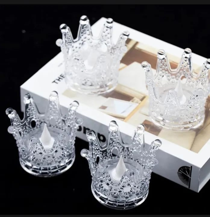 Four glass crown-shaped candle holders with candles on a white box background.