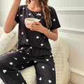Person wearing black pajama set with white heart patterns, sitting on a couch holding a pink cup.