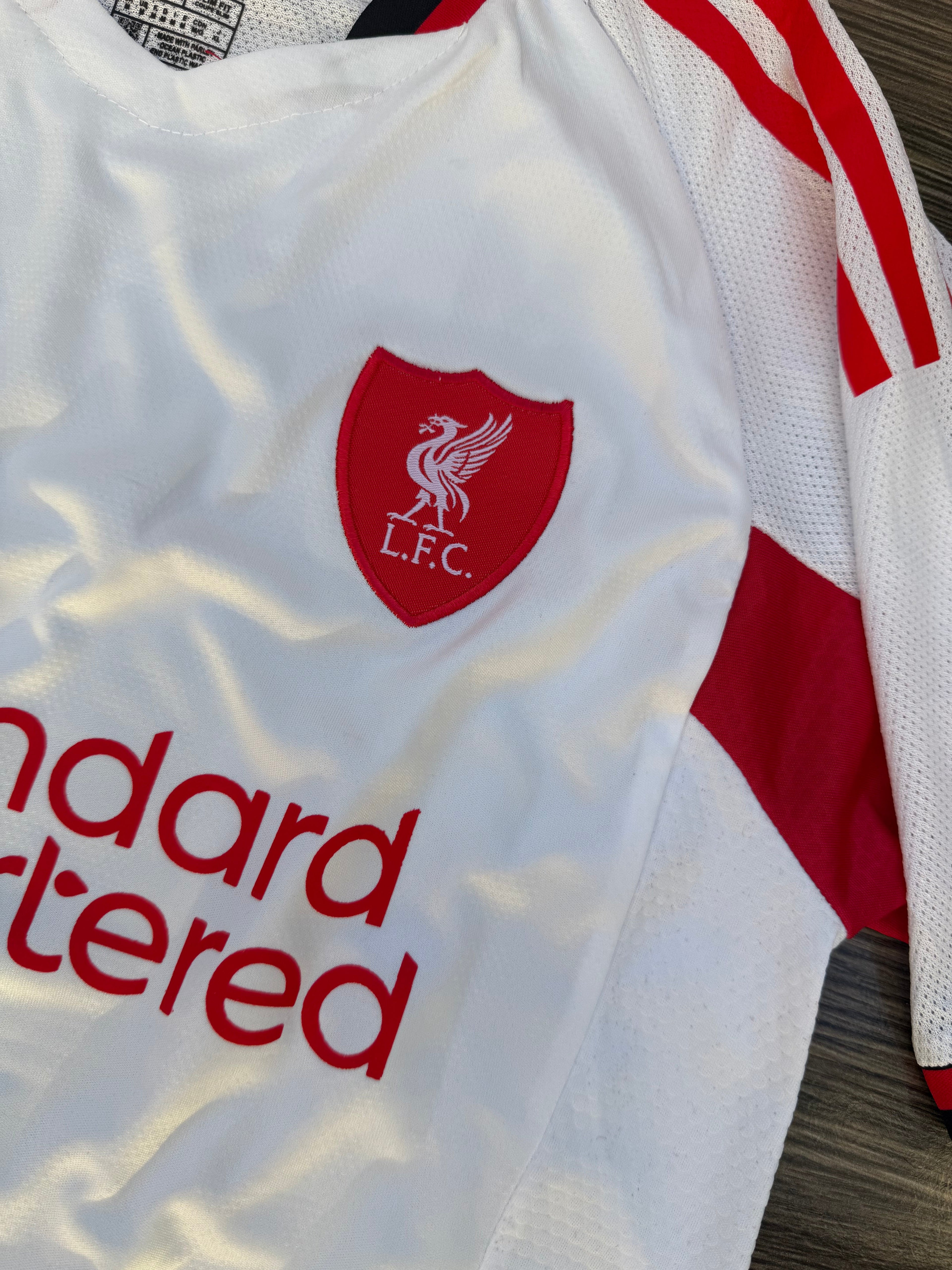 White sports jersey with red accents and a logo, featuring 'L.F.C.' text.