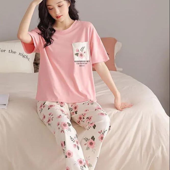 Woman wearing pink pajama top and floral pants sitting on a bed.