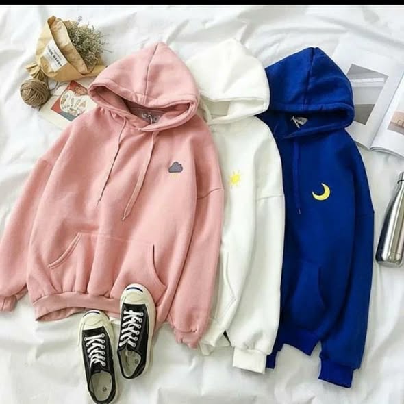 Three hoodies in pink, white, and blue on a bed with sneakers.