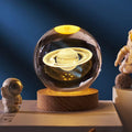 Glass sphere with Saturn model on a wooden base against a dark blue background