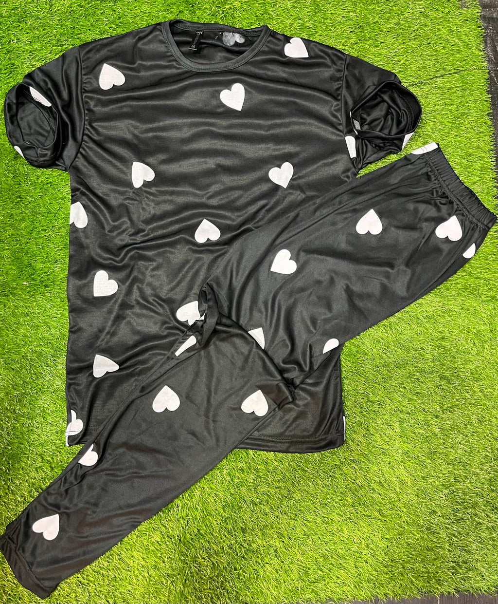 Black pajama set with white heart patterns on a green surface