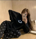 Person wearing a black hoodie with smiley face patterns sitting on a bed.