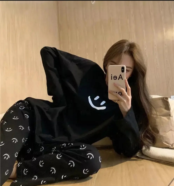 Person wearing a black hoodie with smiley face patterns sitting on a bed.