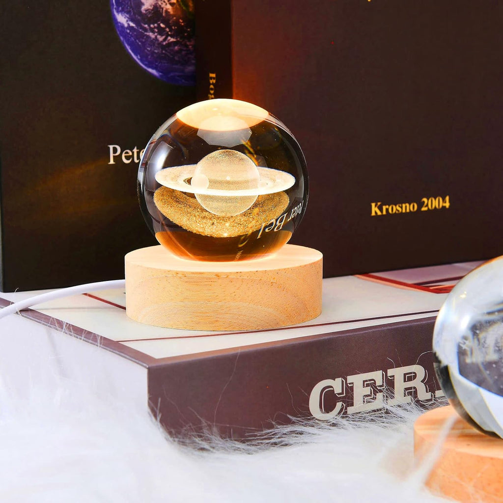 Glass sphere with planetary design on a wooden base, placed on a book with 'Cer' branding.