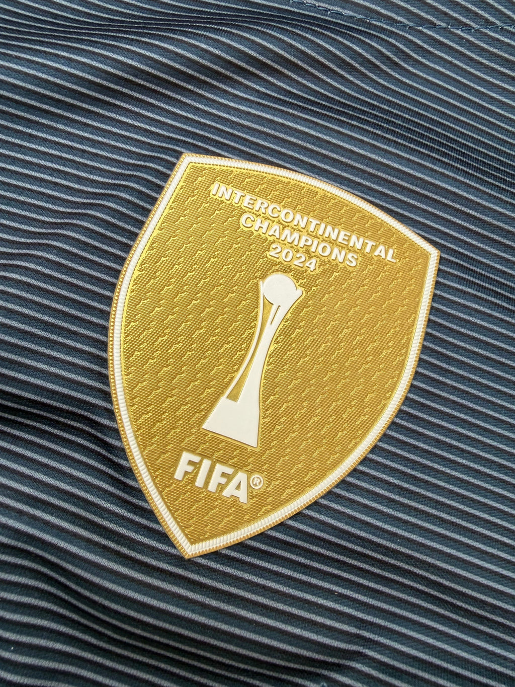 Gold FIFA Intercontinental Champions 2024 patch on a textured fabric background