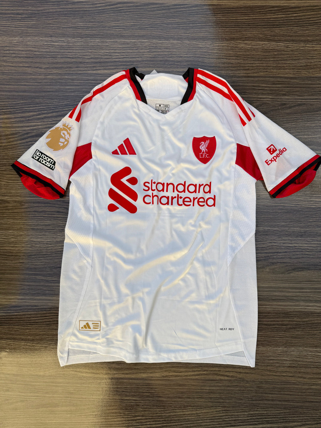 White sports jersey with red accents and branding on a wooden surface