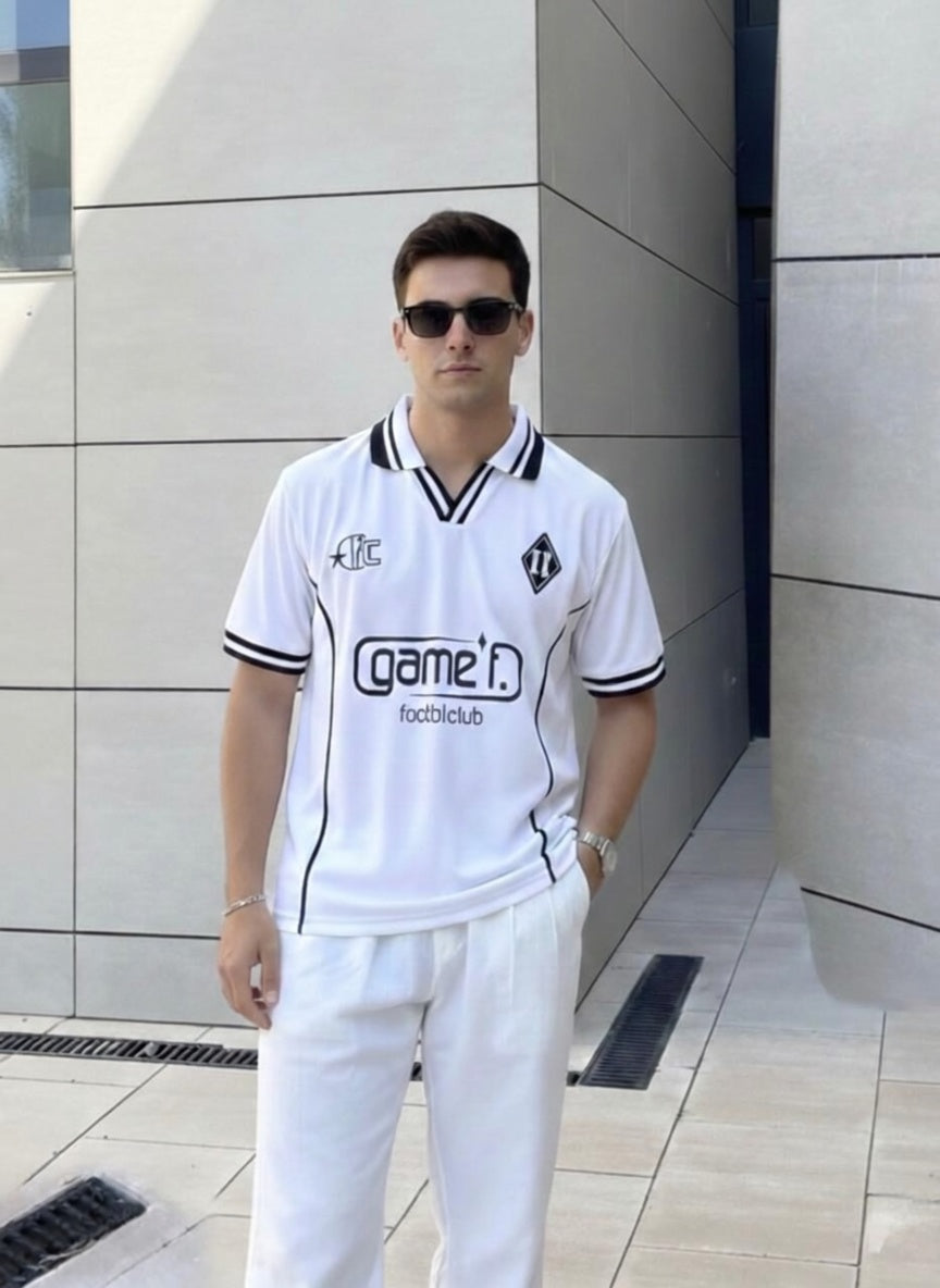 Man wearing a white sports outfit with 'game' logo in front of a modern building.