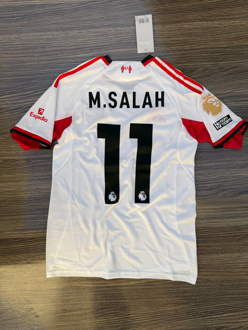 White sports jersey with red accents and 'M. Salah 11' printed on a wooden surface