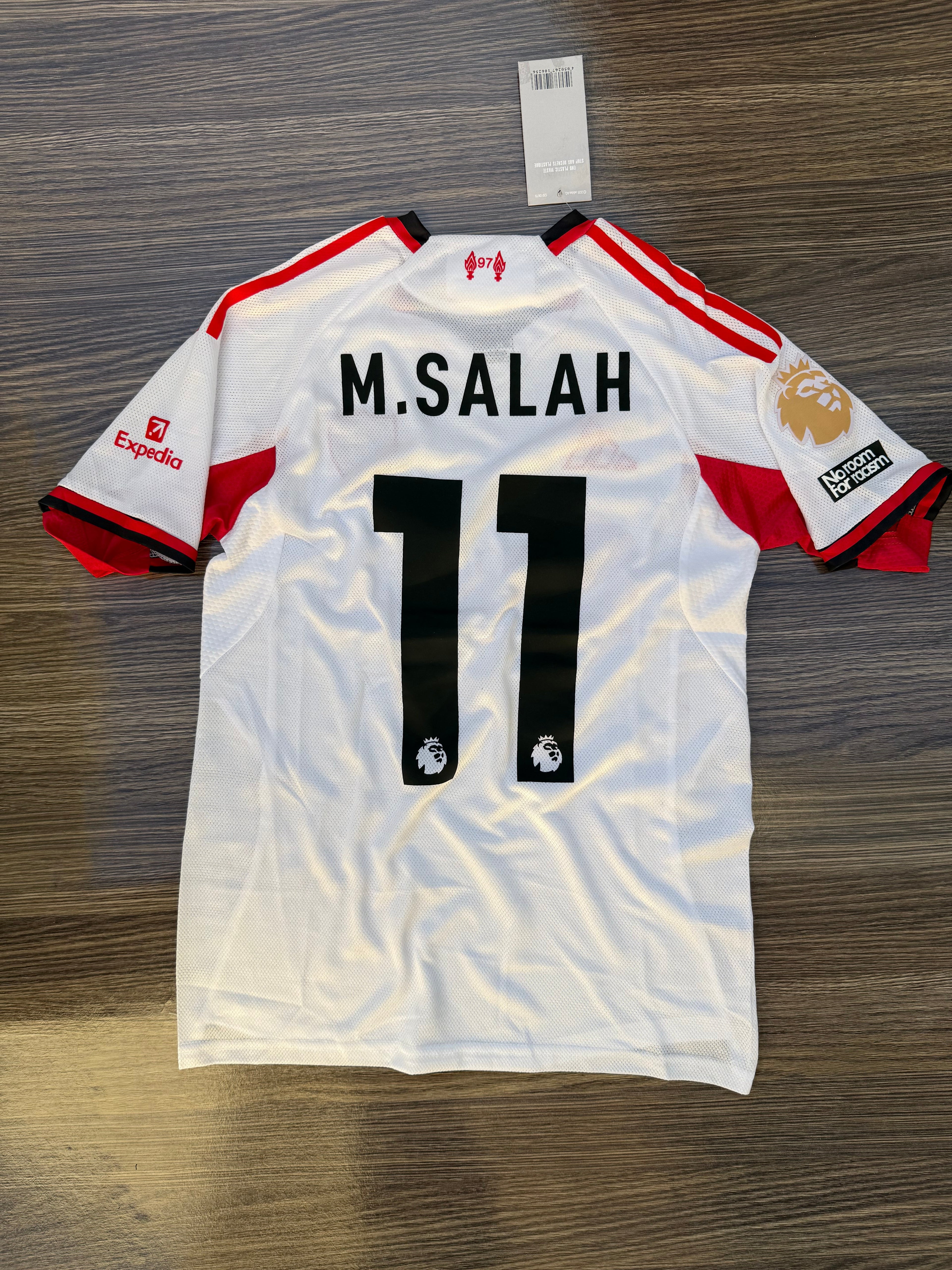 White sports jersey with red accents and 'M. Salah 11' printed on a wooden surface