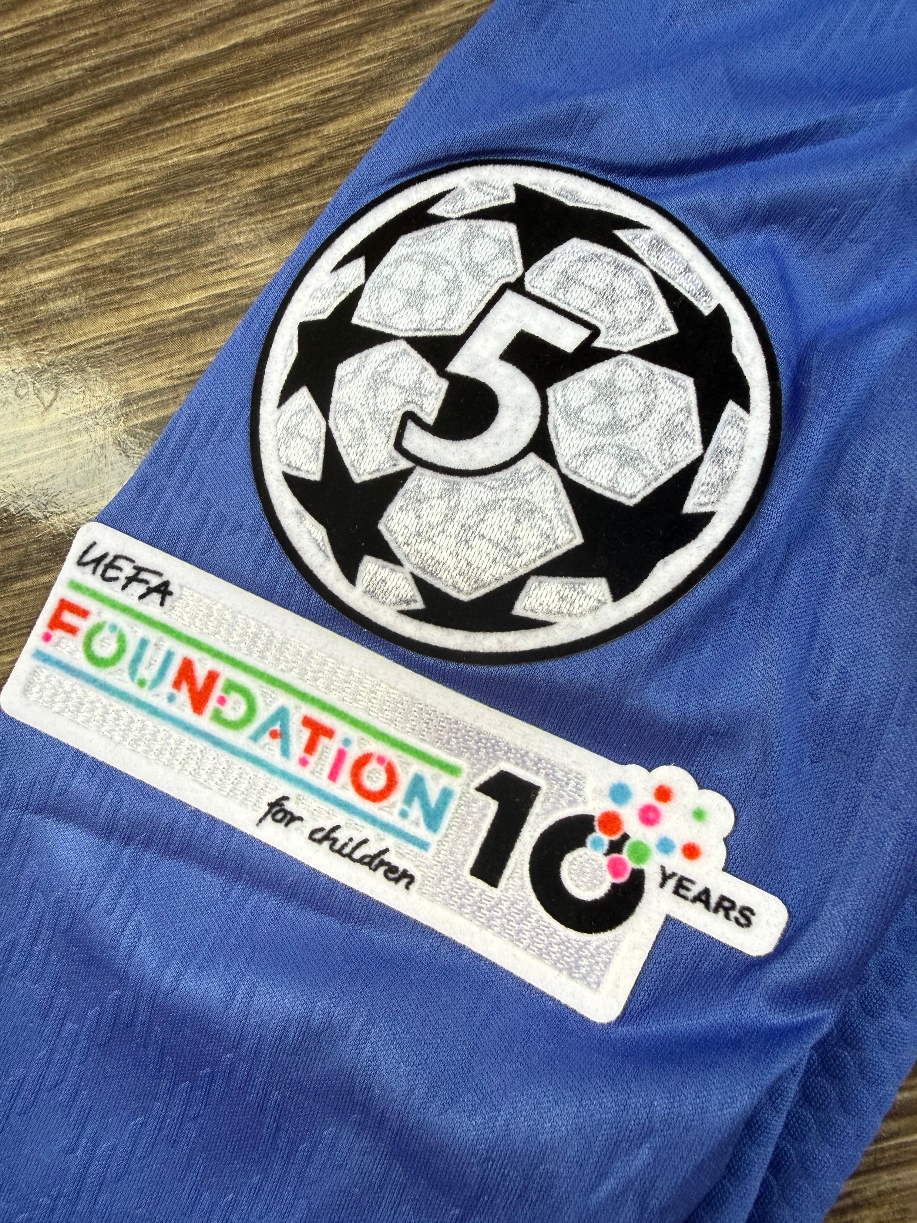 Blue sports jersey with UEFA Foundation for Children patch on a wooden surface