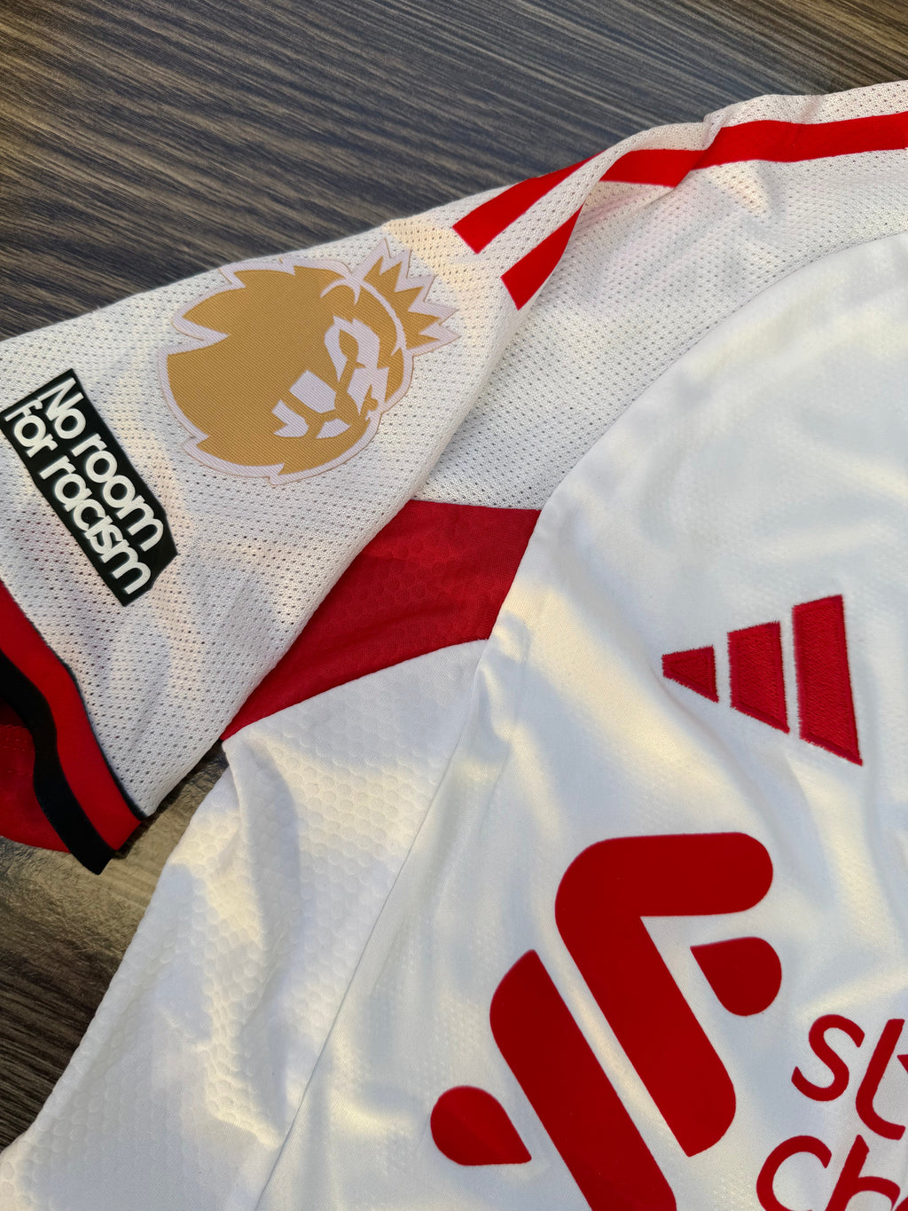 White sports jersey with red and black accents, featuring logos on a wooden surface.
