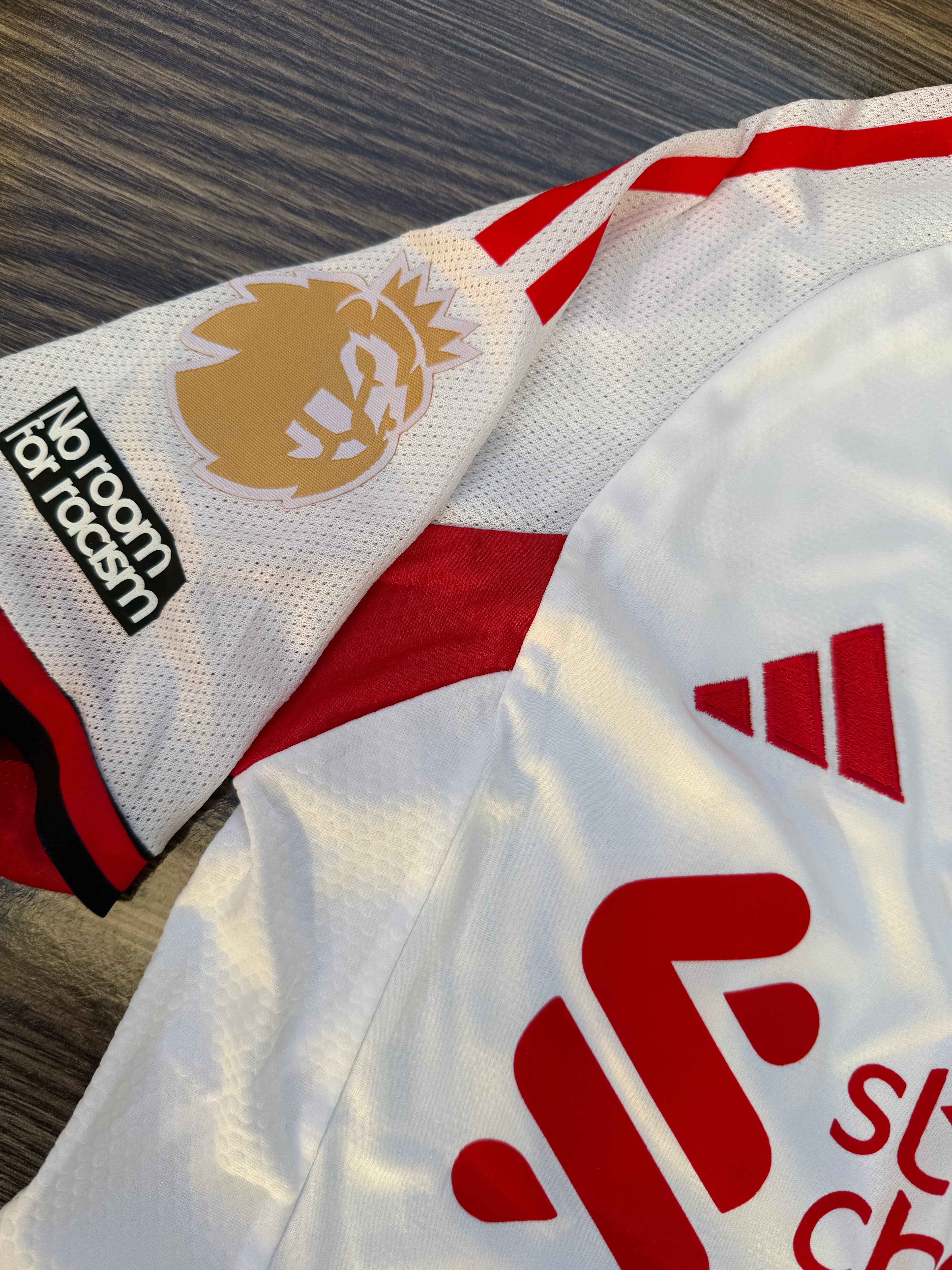 White sports jersey with red and black accents, featuring logos on a wooden surface.
