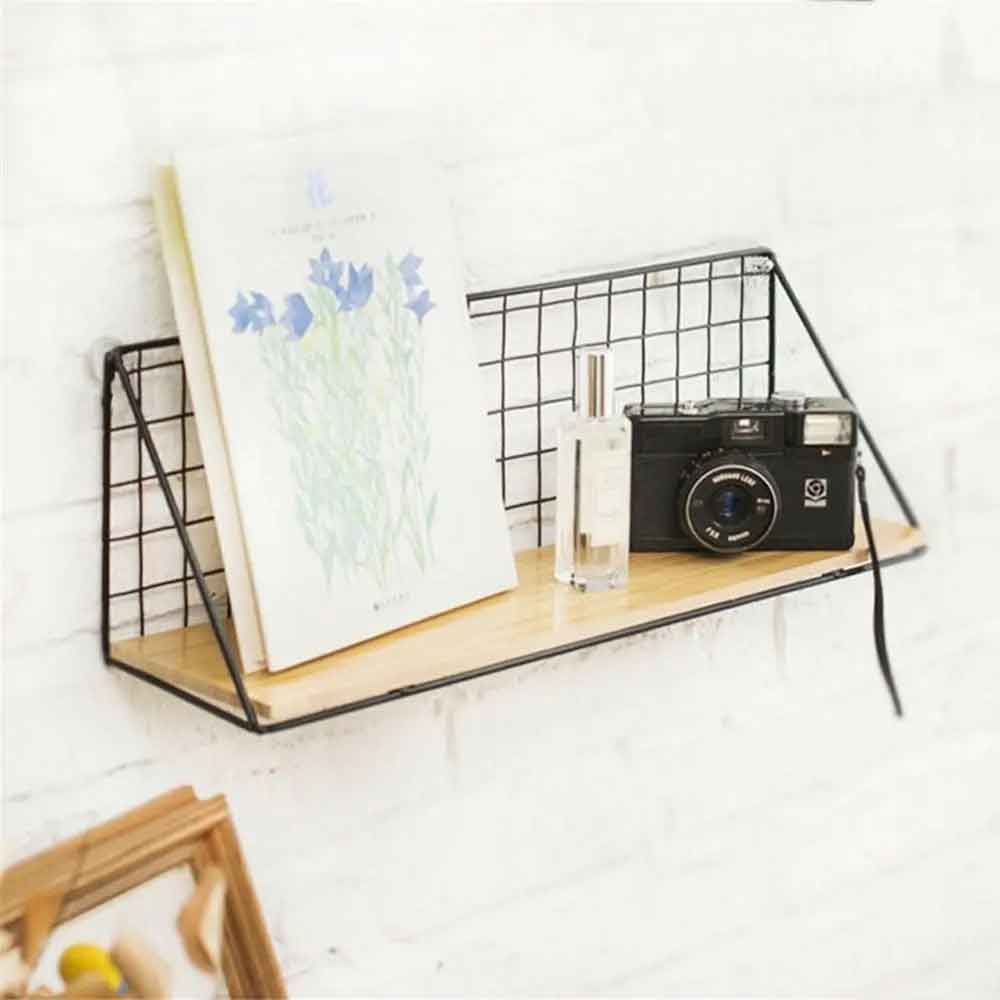 Wall-mounted shelf with a camera, flowers, and a bottle on a white wall.