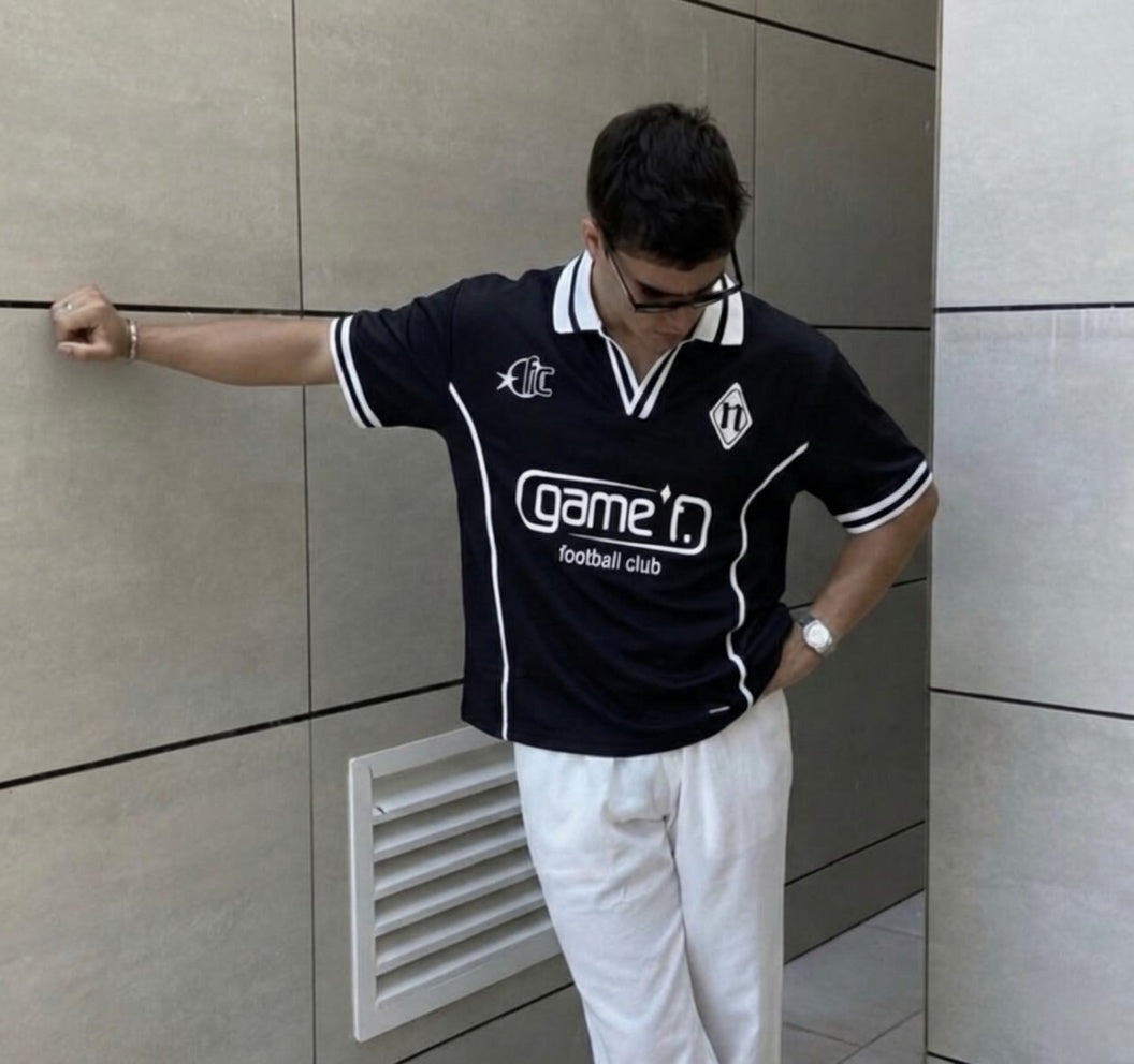 Person wearing a black sports jersey with visible branding against a tiled wall.