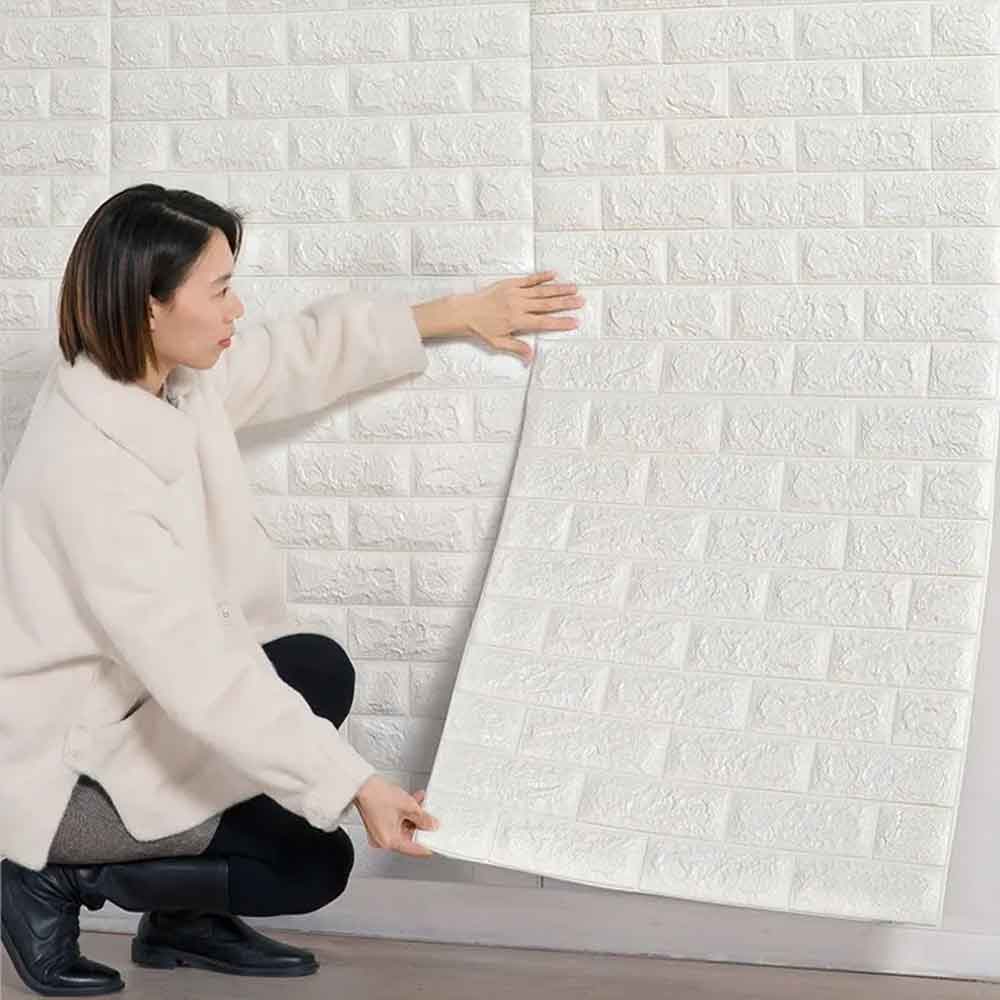 Woman installing white brick-patterned wall panels on a wall.