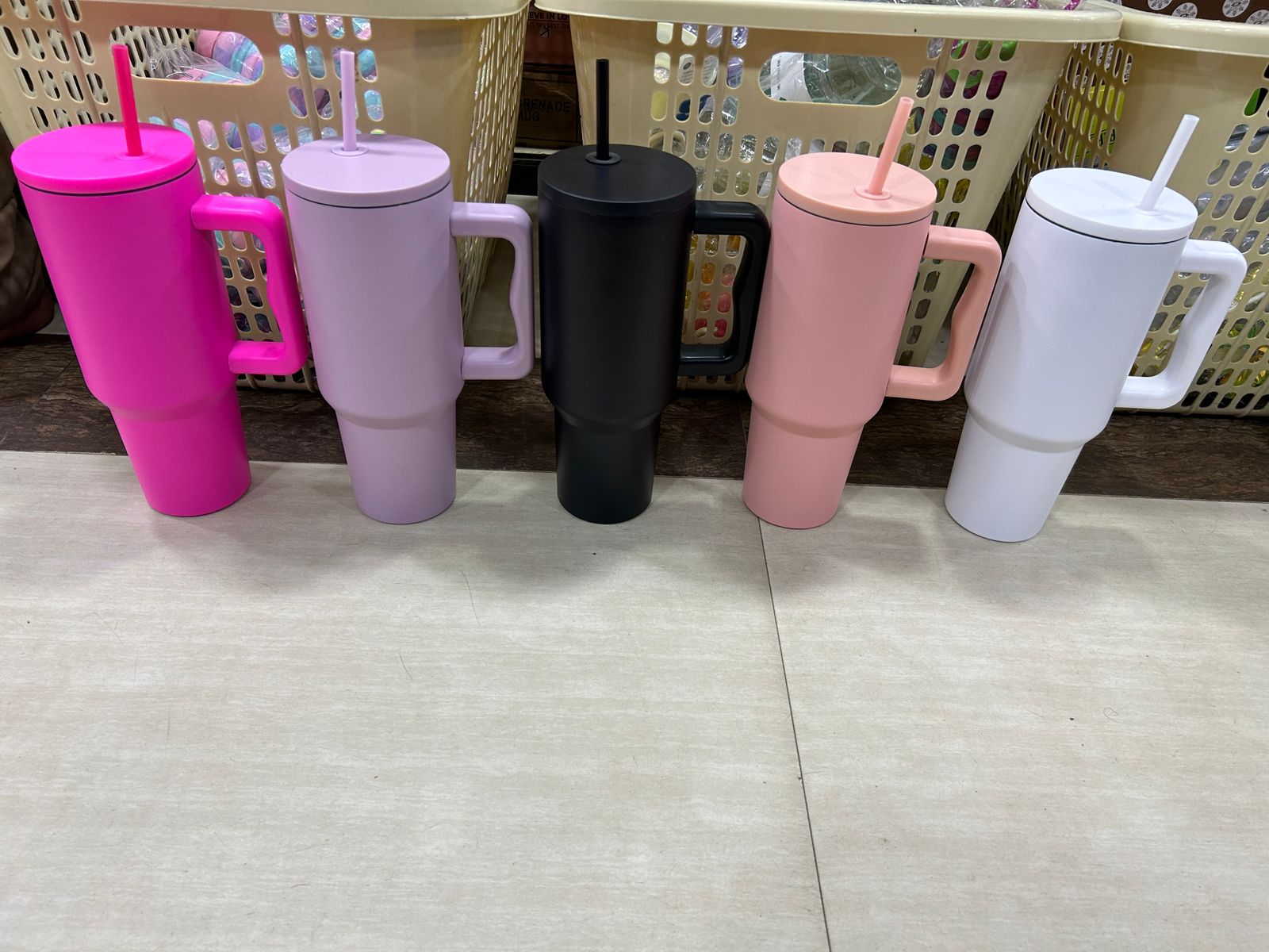 Set of colorful tumblers with handles and straws on a tiled floor.
