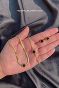 Gold necklace with black stones held in a hand against a dark fabric background