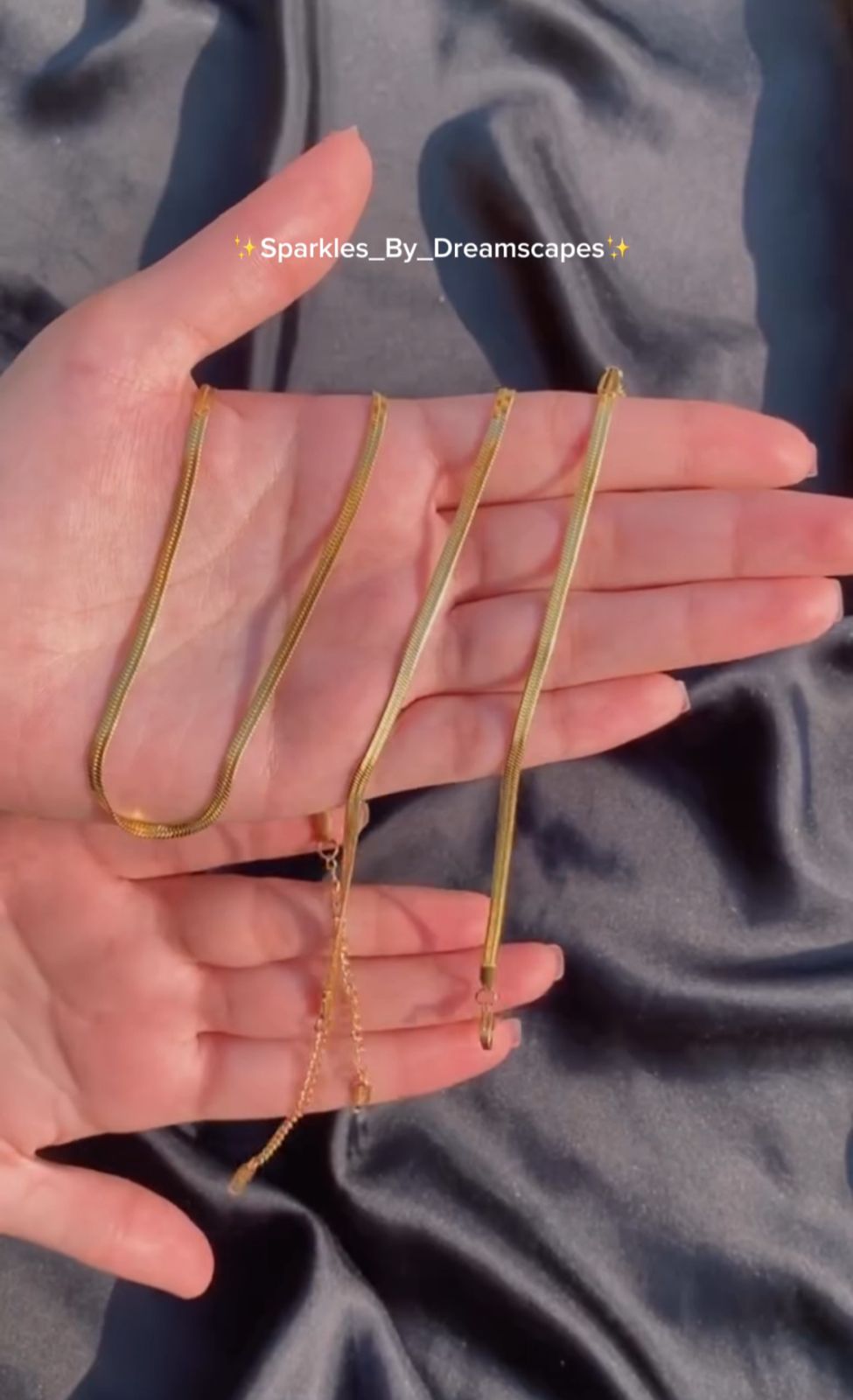 Gold jewelry on a hand with a dark fabric background