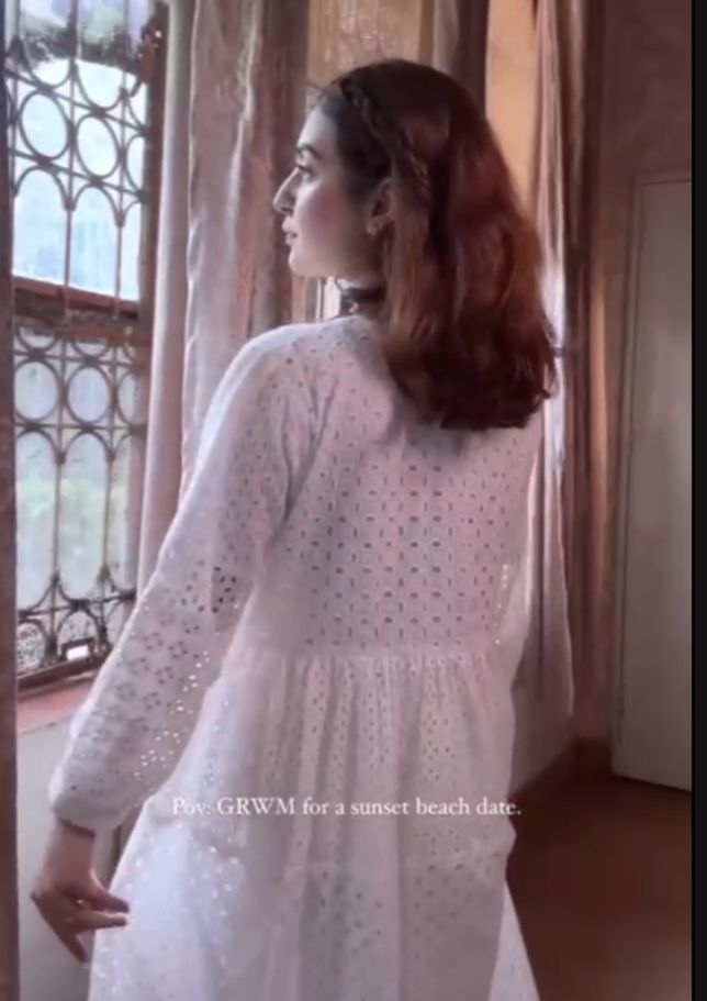 Woman in a white outfit standing by a window with decorative iron bars.