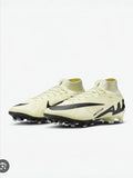 Pair of light-colored soccer cleats with a black swoosh logo on a white background