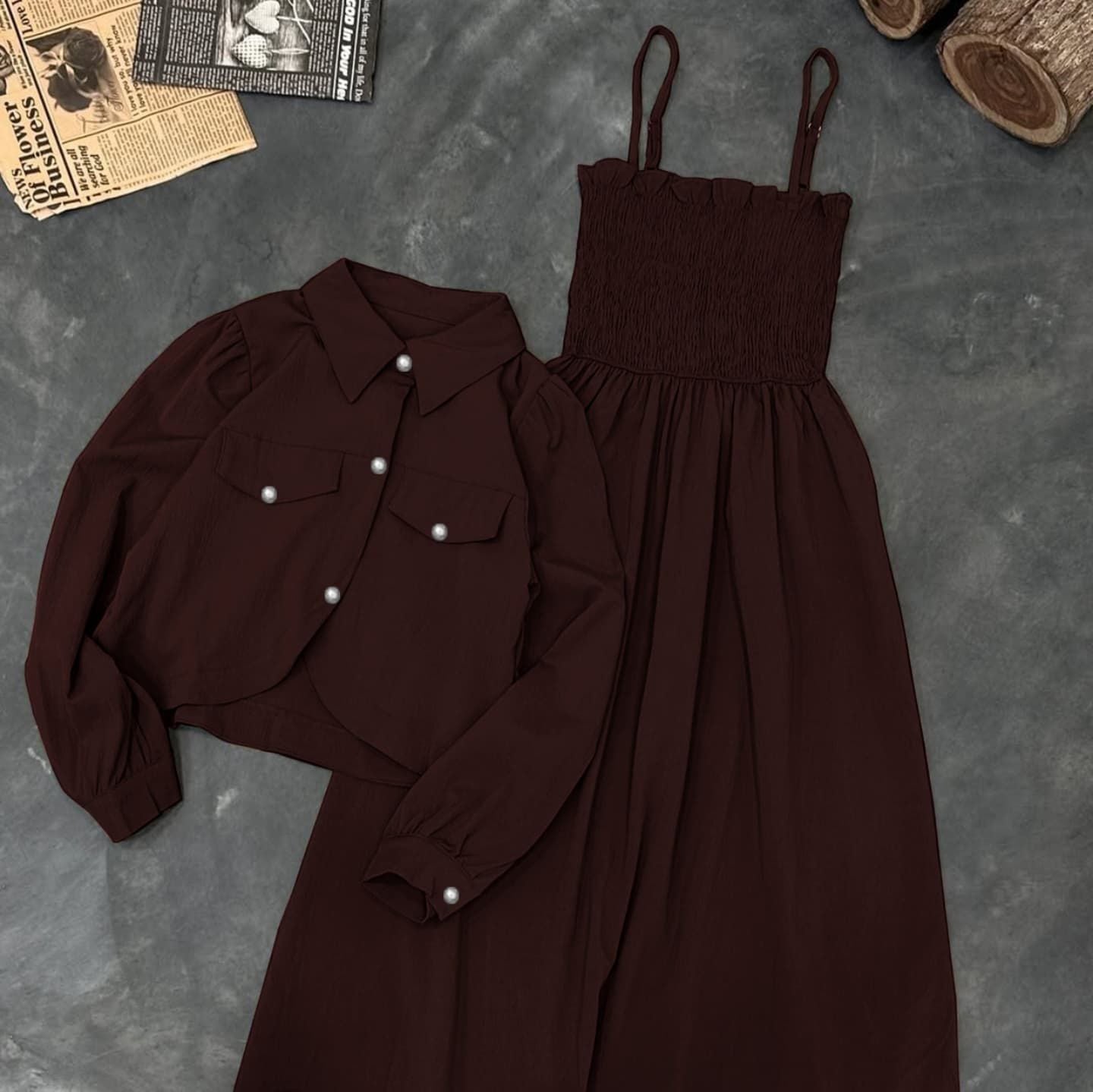 Brown shirt and dress set on a textured gray surface with a newspaper and logs in the background.