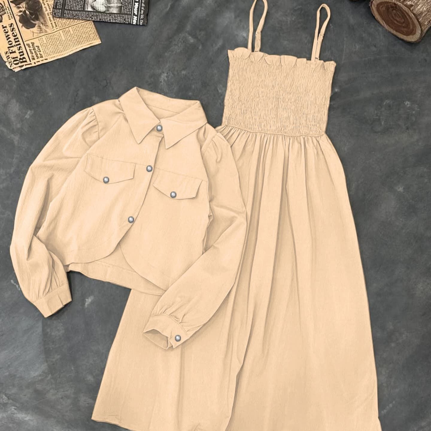 Beige shirt and dress set on a textured surface with a newspaper and log in the background.