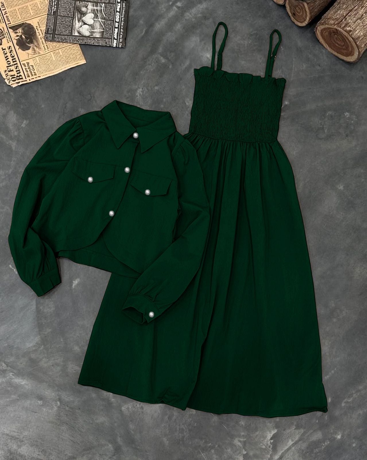 Green shirt and dress on a textured gray surface with wooden logs and newspaper.