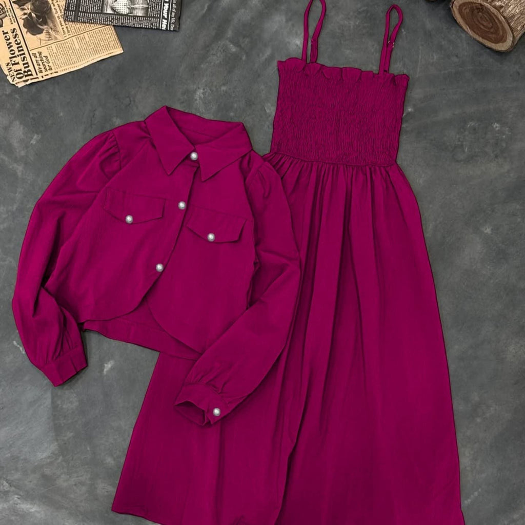 Magenta shirt and dress set on a gray surface with a newspaper and wooden block in the background.