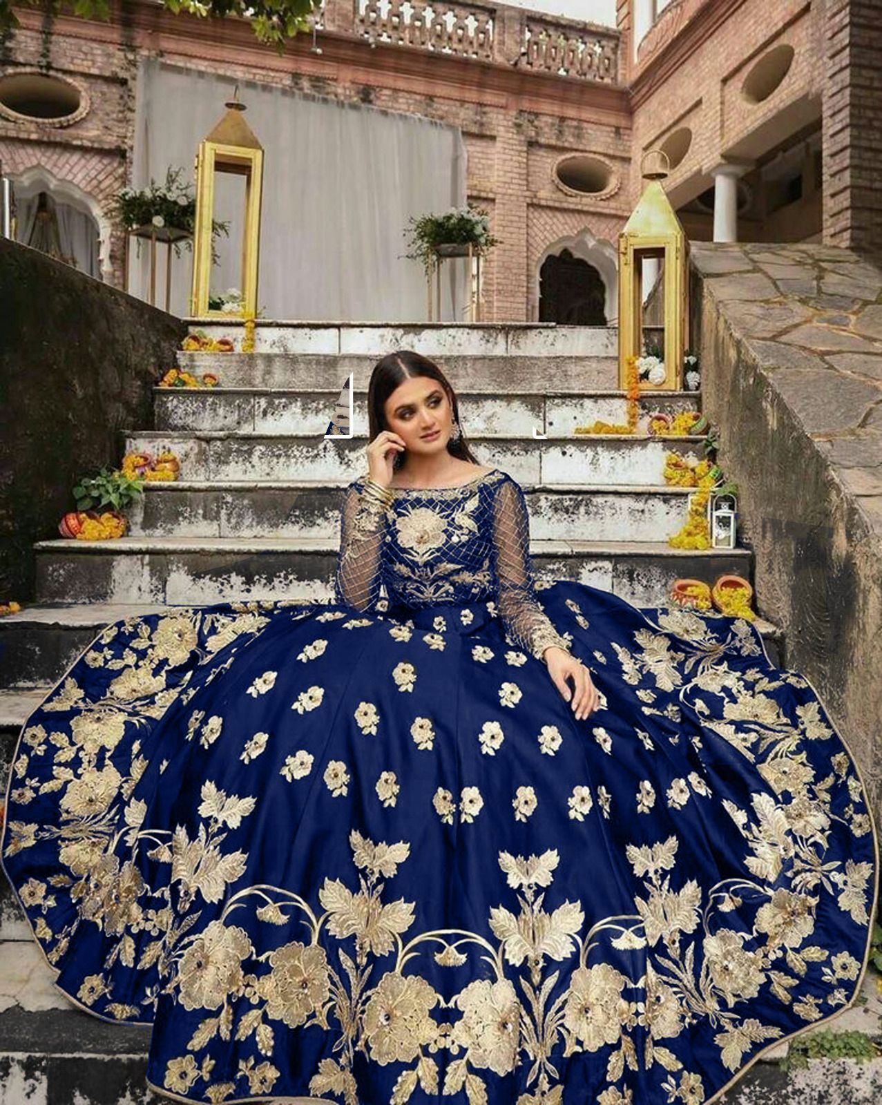 Woman in a blue and gold embroidered dress sitting on stone steps.