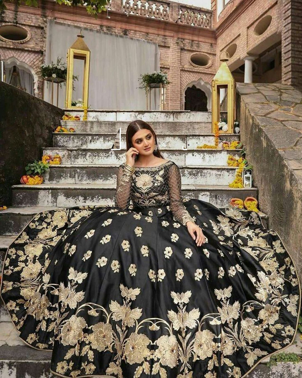 Woman in a black and gold embroidered gown sitting on stone steps.
