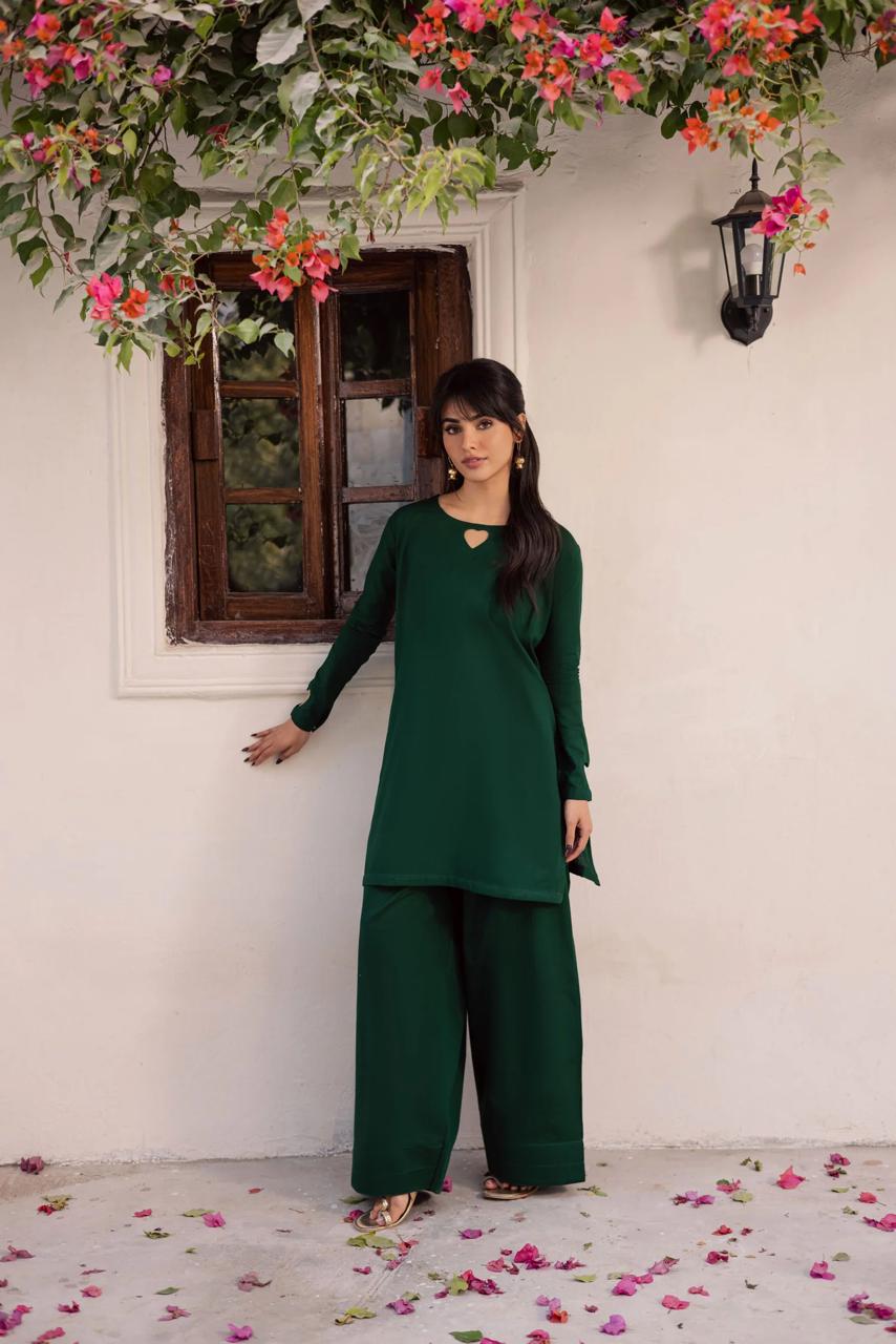 Woman in a green outfit standing against a white wall with floral decorations.