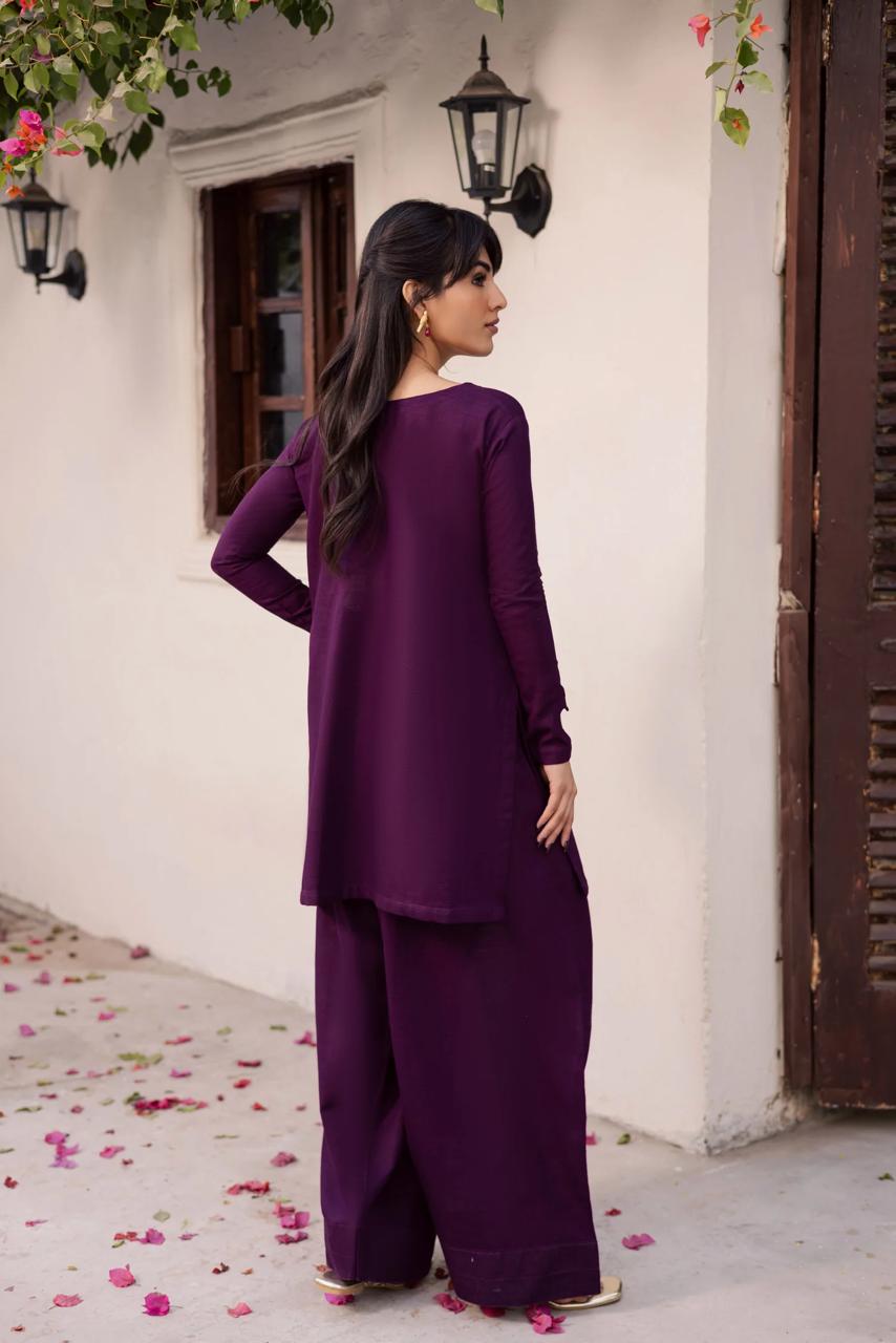 Woman in a purple outfit standing in front of a white wall with floral decorations.