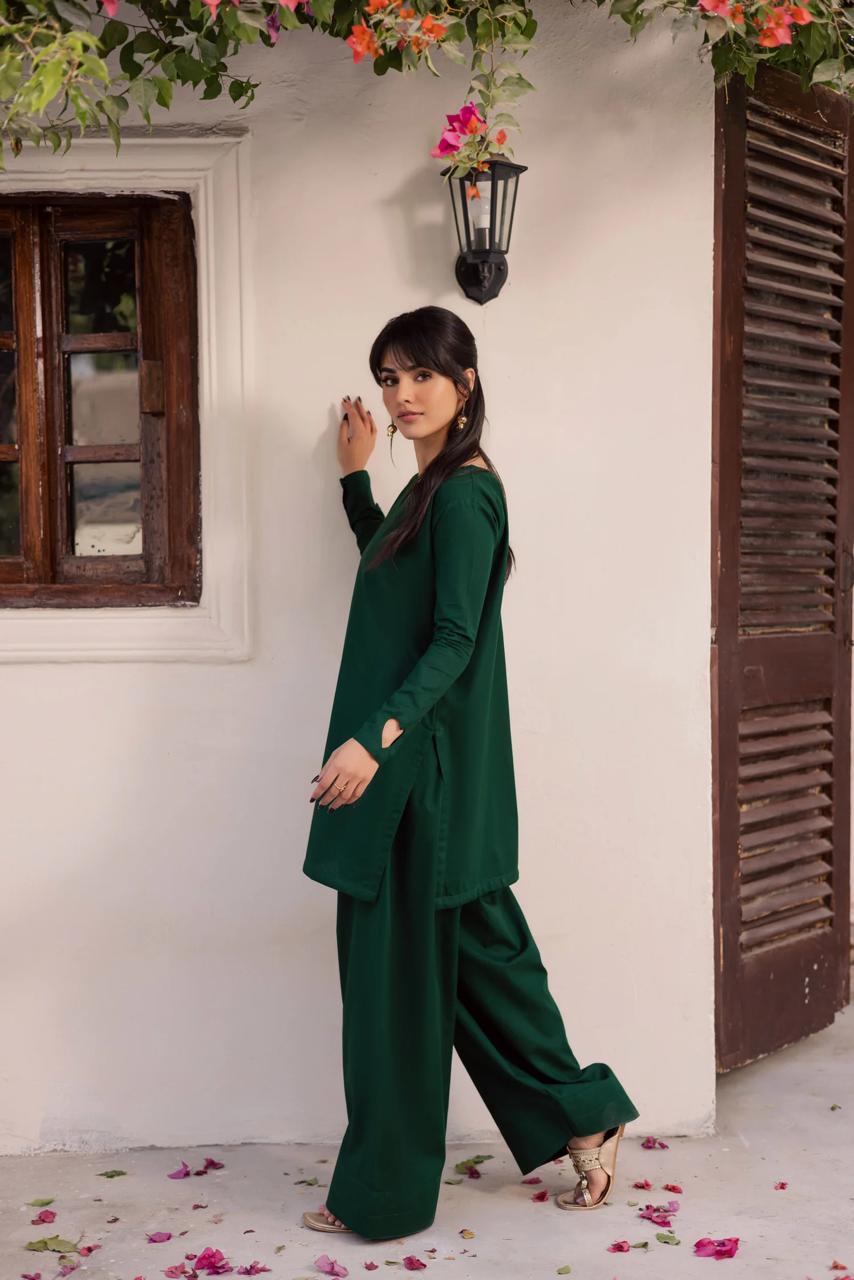 Woman in a green outfit standing against a white wall with floral decorations.