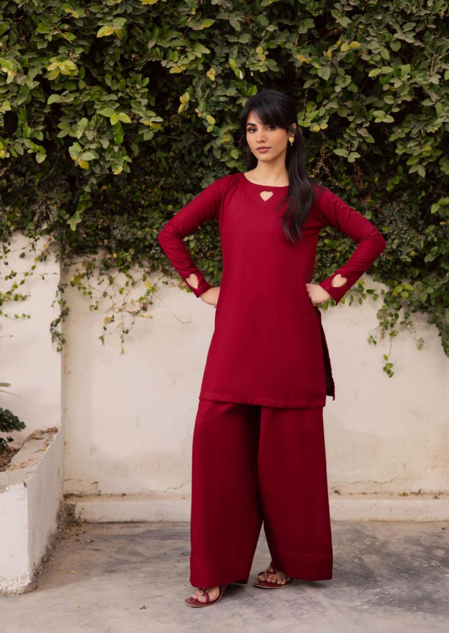 Woman wearing a red traditional outfit standing against a white wall with greenery.