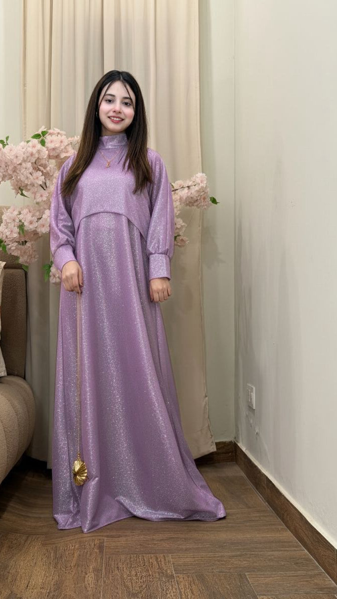 Woman wearing a long purple dress standing indoors with decorative flowers and a couch in the background.