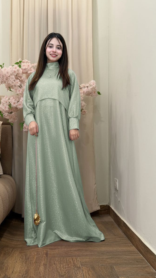 Woman in a long green dress standing indoors with decorative flowers in the background