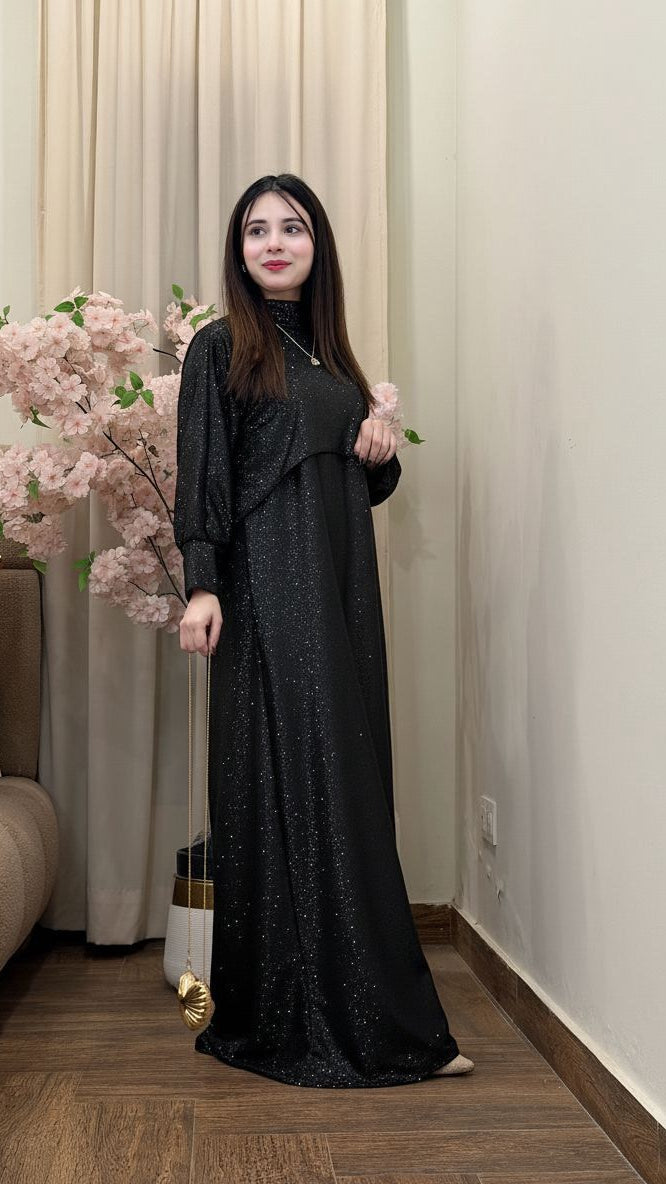 Woman in a long black dress standing indoors with decorative elements.