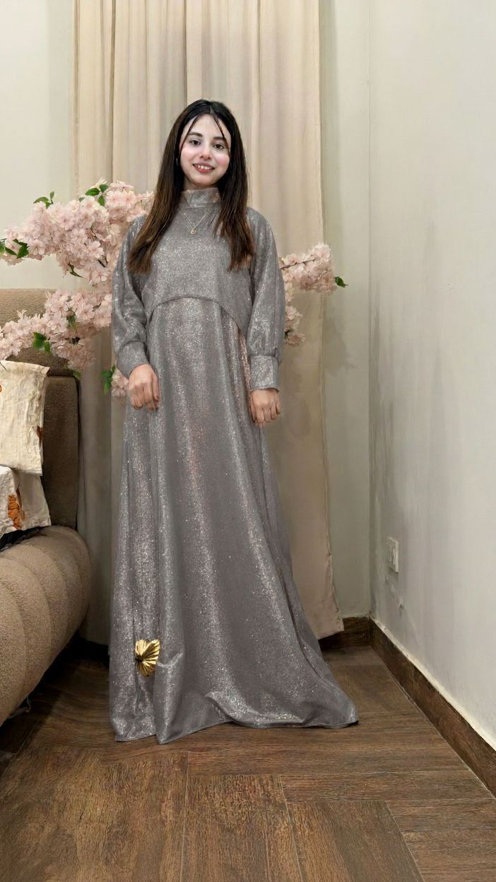 Woman in a long gray dress standing in a room with light-colored curtains and a couch.