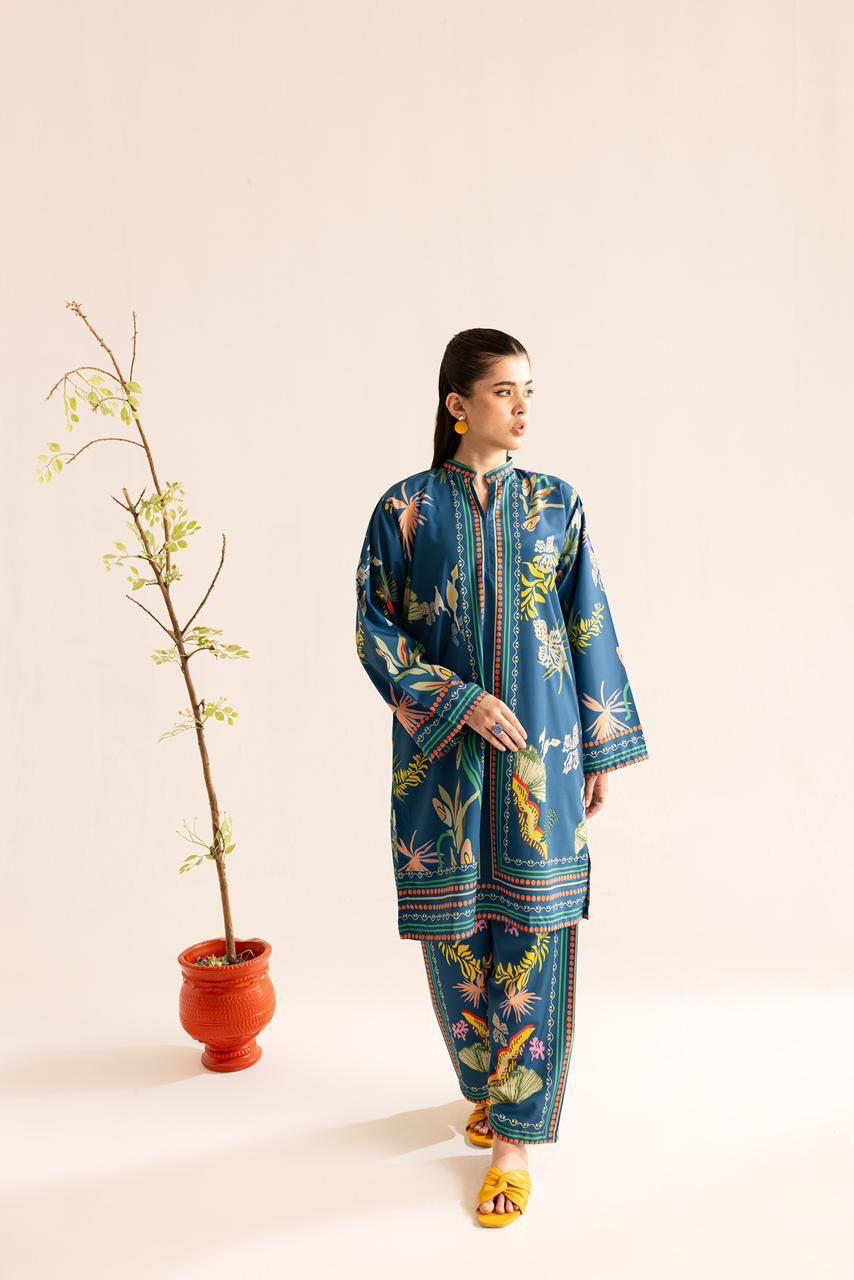 Woman wearing a blue floral traditional outfit standing next to a potted plant on a beige background