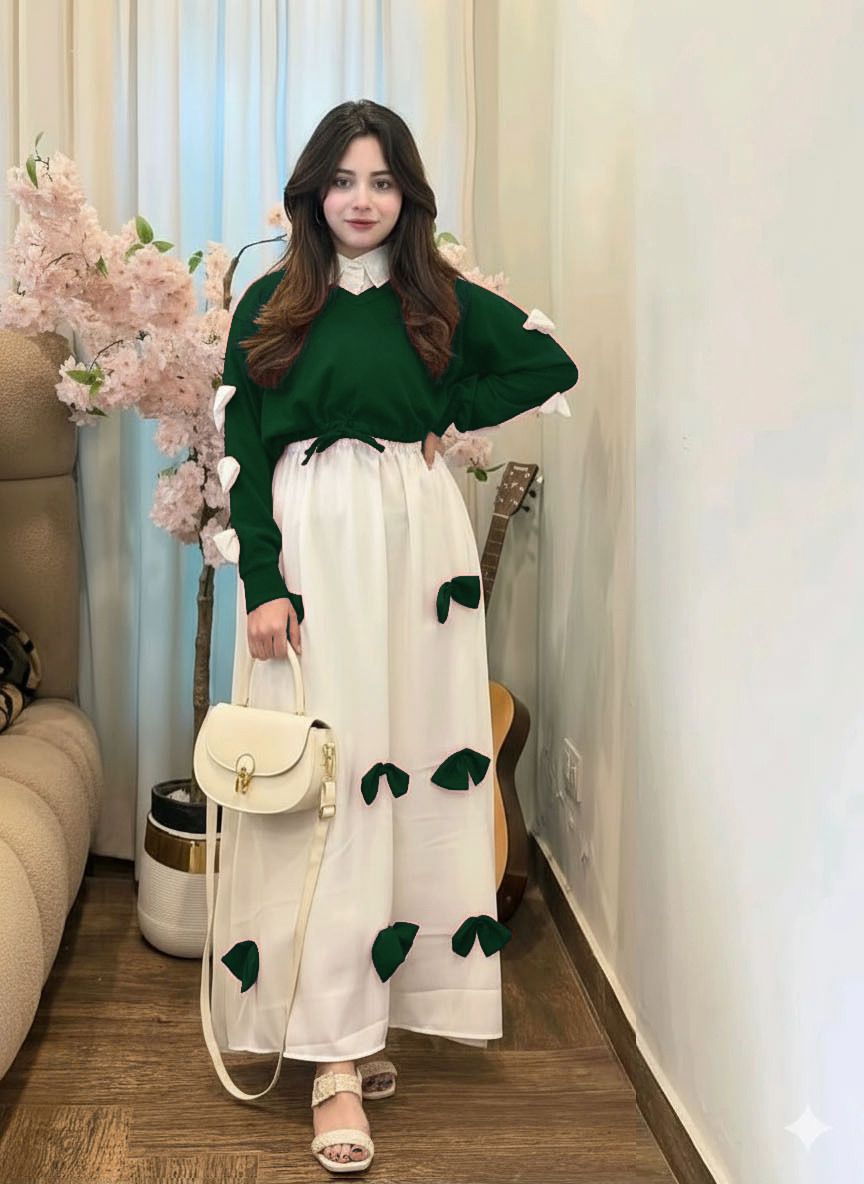 Woman in a green sweater and white dress with green accents standing in a room with flowers and furniture.