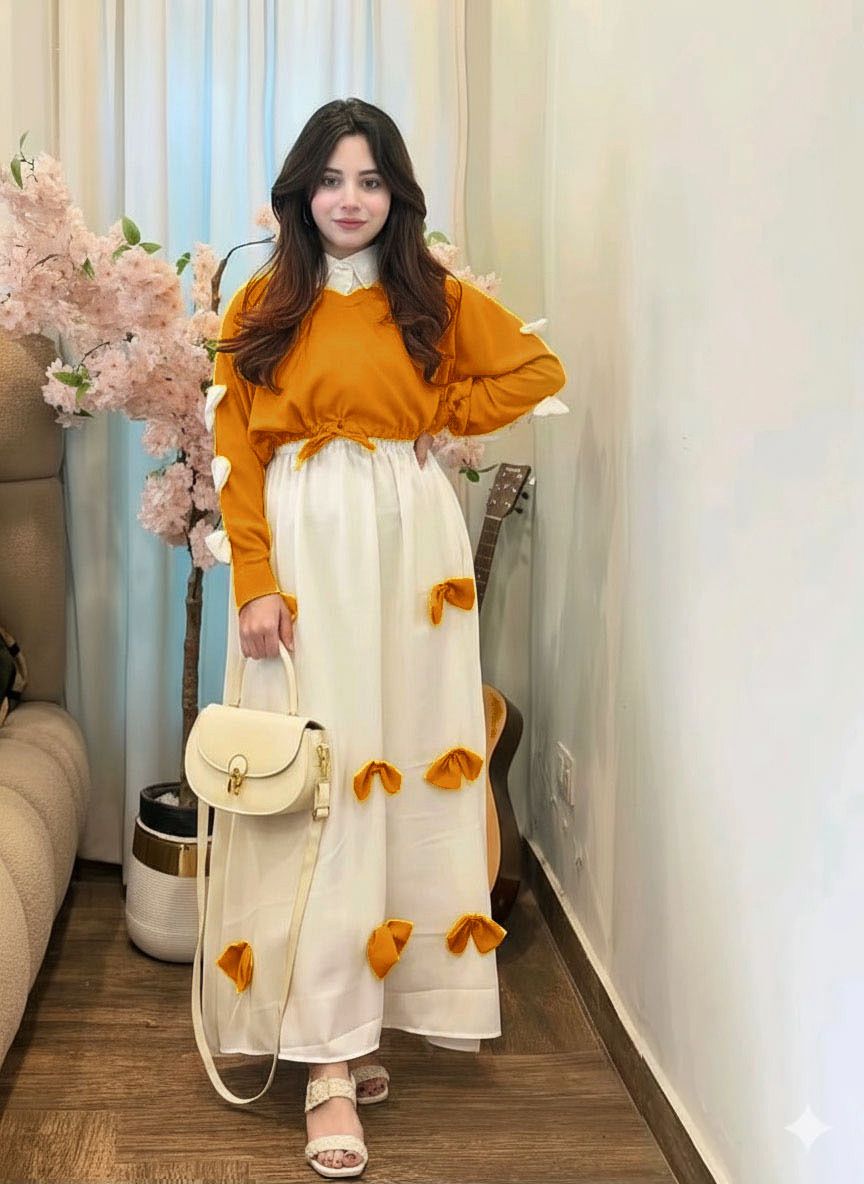 Woman in mustard yellow top and white dress with orange flowers standing in a room with floral decorations.