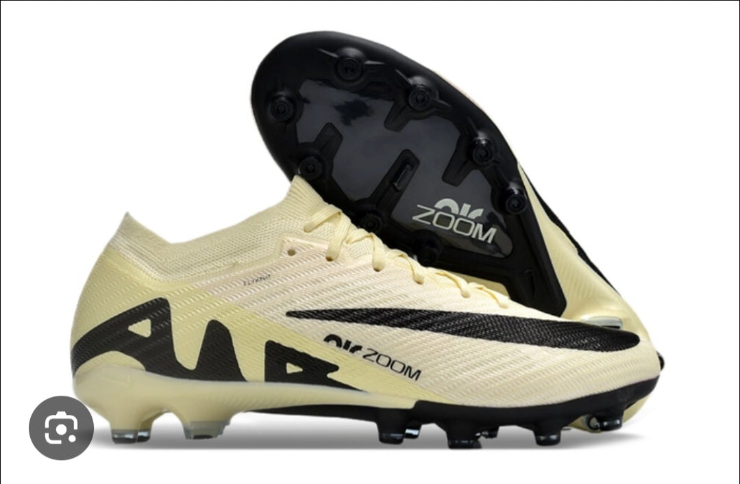 Beige soccer cleats with black accents and 'Air Zoom' branding on a white background