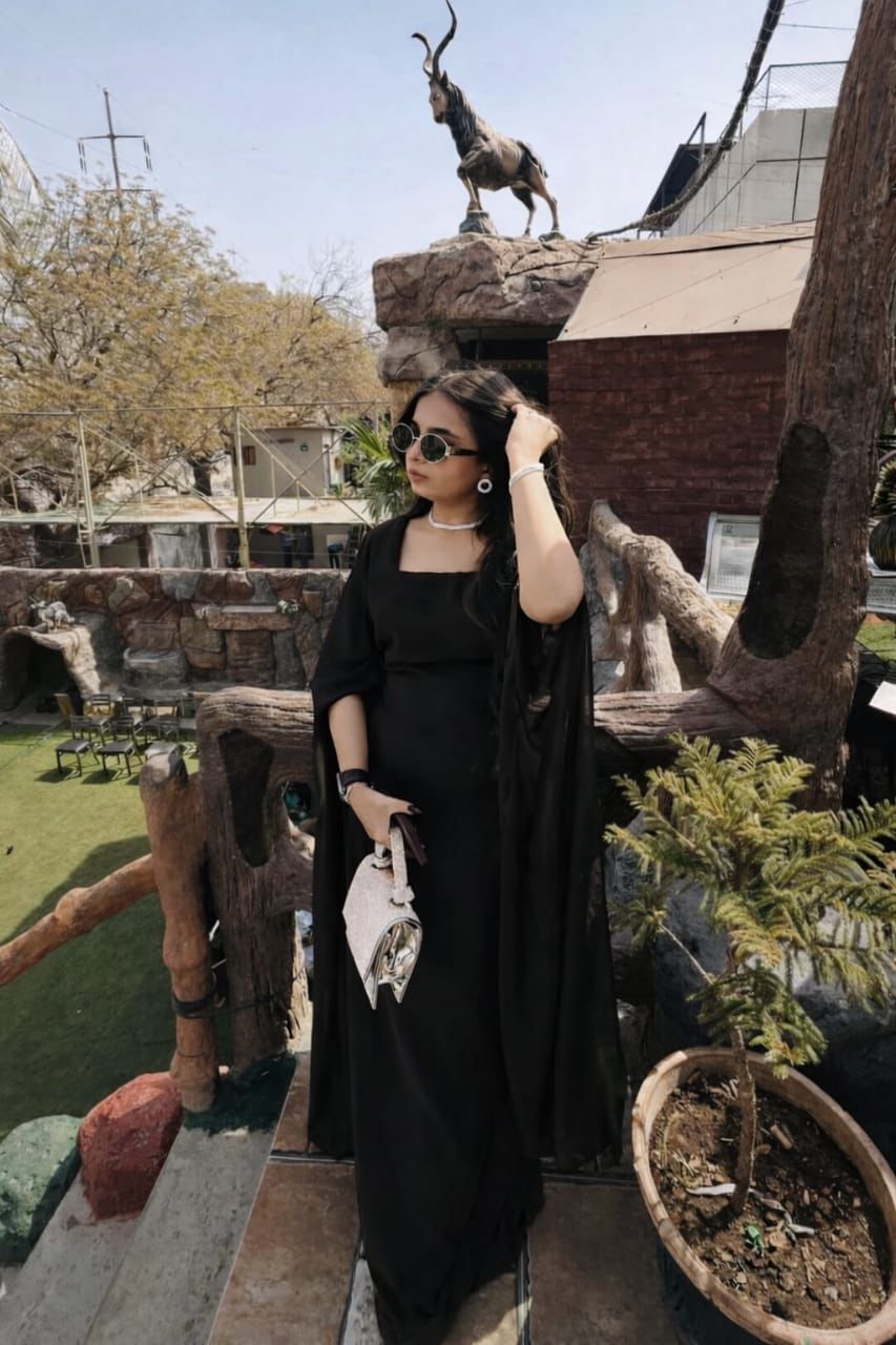 Woman in a black dress standing in front of a zoo enclosure with animals.