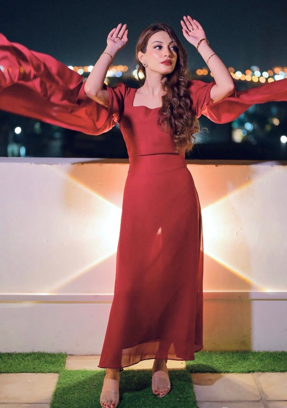 Woman in a red dress standing on a rooftop with city lights in the background