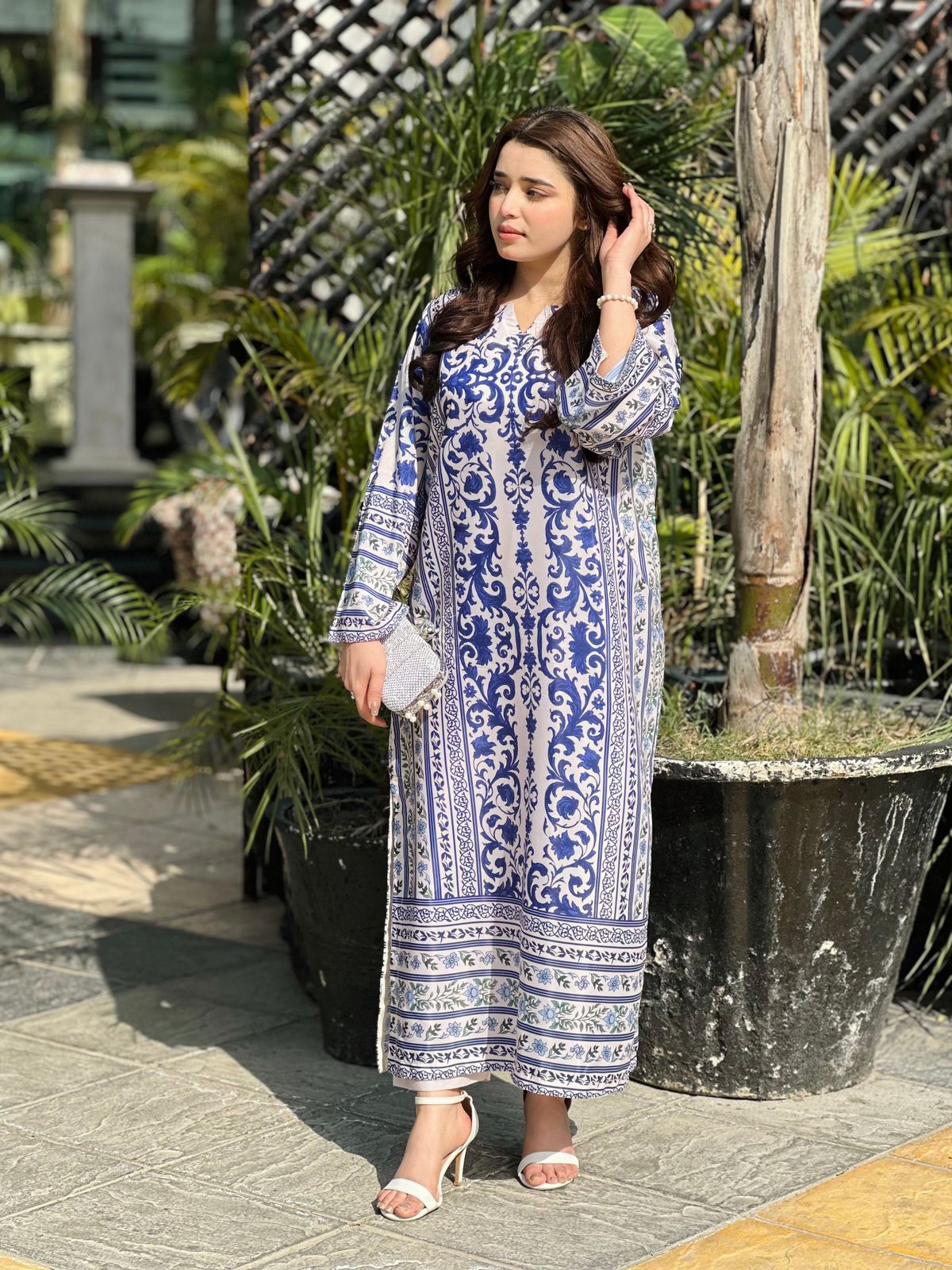Woman wearing a blue and white patterned dress standing outdoors with plants in the background