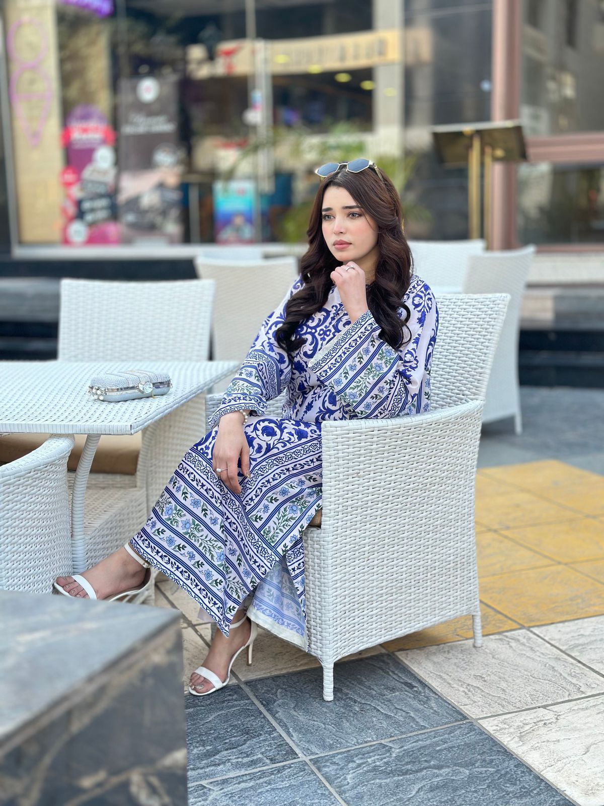Woman in a blue patterned dress sitting outdoors on a chair.