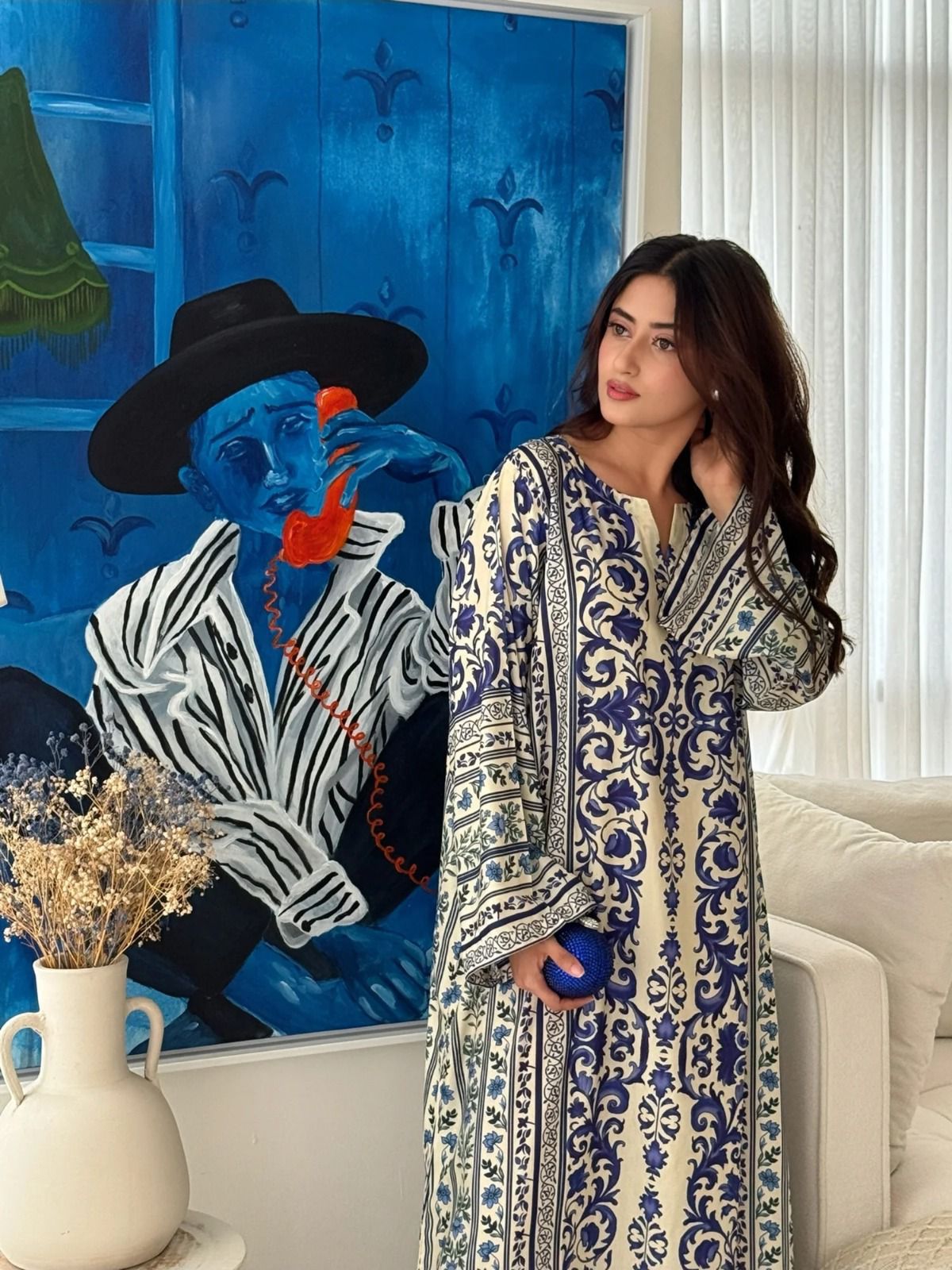 Woman in a patterned dress standing in a room with a colorful painting on the wall.