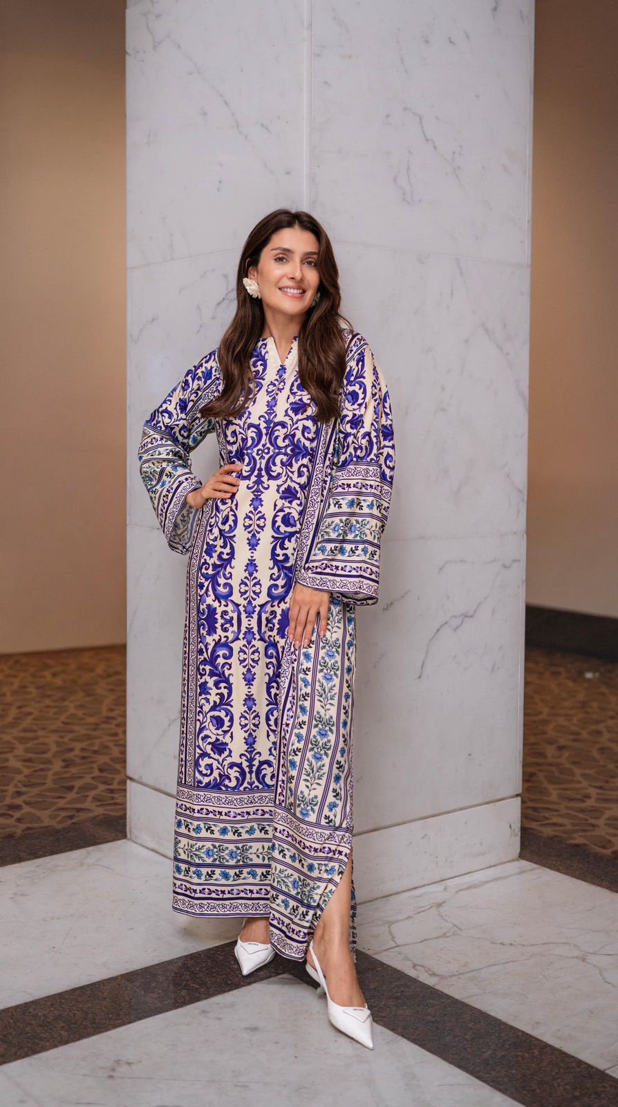 Woman in a patterned dress standing against a marble wall.